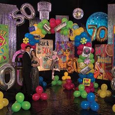 a man and woman standing in front of an entrance decorated with balloons, streamers and disco balls