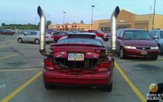 the back end of a red car with its hood up in a parking lot next to other cars