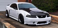 a white mustang with black stripes parked in front of a garage door on the street