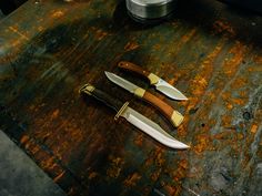 two knives sitting on top of a wooden table next to an open cannister