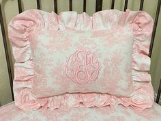 a pink and white bed with a monogrammed pillow on it's back