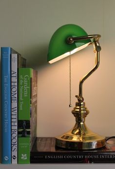 a green lamp sitting on top of a book shelf next to a stack of books