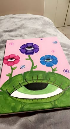 an art project with flowers painted on the side of a piece of paper that is laying on a bed