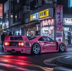 a pink sports car parked on the side of a road in front of buildings at night