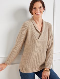 a woman leaning against a wall wearing a sweater