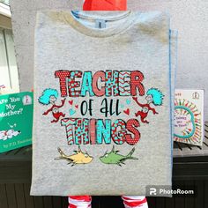 a person holding up a t - shirt with the words teacher of all things on it