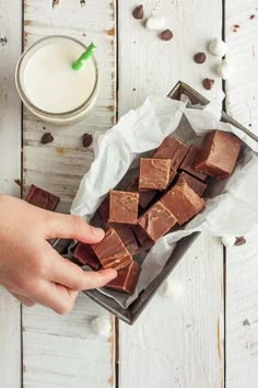 someone is holding a piece of chocolate next to a glass of milk and some nuts