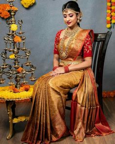 a woman sitting on top of a chair wearing a gold and red sari dress