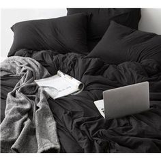 an open laptop computer sitting on top of a black bed covered in blankets and pillows