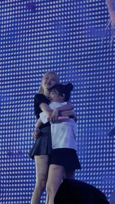 two girls hugging each other on stage with blue lights in the back ground behind them