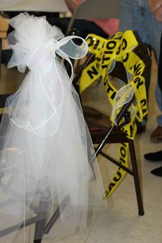 a chair with a white tulle and bow tied to it's back sitting in front of a group of people