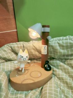 a cat figurine sitting on top of a bed next to a wooden lamp