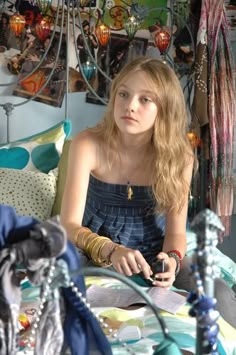 a young woman sitting on top of a bed next to a purse and jewelry rack