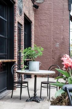 an outdoor table with two chairs and a potted plant