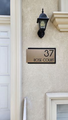 a house number sign mounted to the side of a white building with a light on it