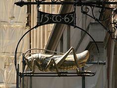 a metal sign with a large insect on it's side hanging off the side of a building