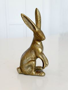 a gold colored rabbit statue sitting on top of a table next to a white wall