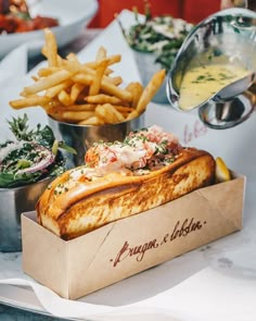 a sandwich in a box with french fries and other food on the table behind it