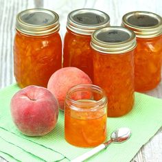 several jars filled with peach jam on top of a green napkin next to an apple