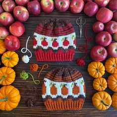 two knitted hats sitting next to pumpkins and apples