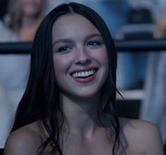 a woman with long black hair smiles at the camera while others sit in the background