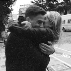 a man and woman hugging each other in front of a street with cars behind them