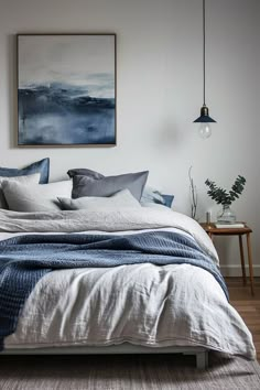 a bed with white sheets and blue pillows in a room next to a painting on the wall