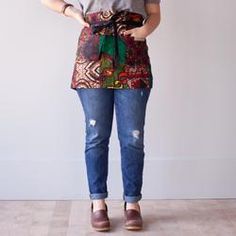 a woman standing in front of a white wall wearing a colorful apron and shoes with her hands on her hips