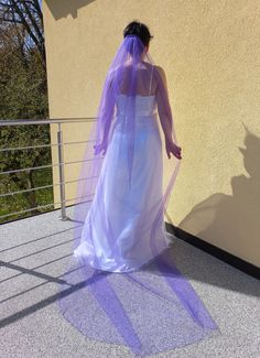 a woman in a white dress and purple veil walking up stairs with her hand on the railing