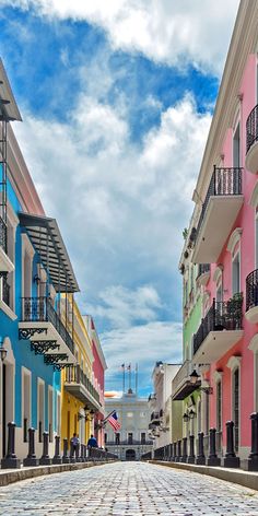 an empty cobblestone street lined with multi - colored buildings and balconies