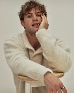 a man in a white coat sitting on a stool with his hand to his face