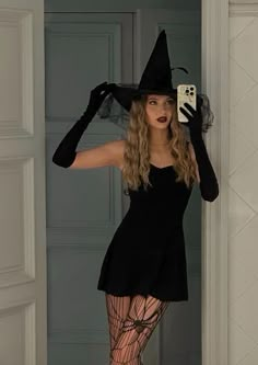 a woman in a black dress and hat holding a cell phone