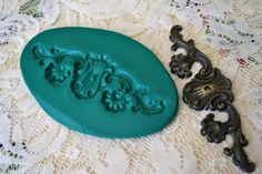 a green cookie mold sitting on top of a lace covered tablecloth next to an ornate cast iron door handle