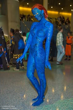 a woman with blue paint on her body is standing in the middle of a crowd