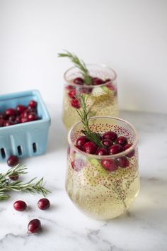 two glasses filled with cranberries and ice on top of a marble countertop