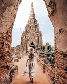 a woman in a white dress and hat walking through an archway to a building that looks like a temple