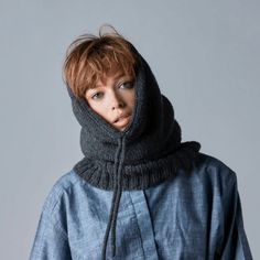 a woman with red hair wearing a blue jacket and black scarf over her head, standing in front of a gray background