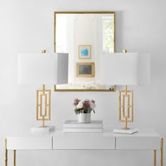 a white console table topped with two lamps and a mirror over it, next to a vase filled with flowers