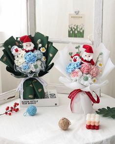 two bouquets of flowers sitting on top of a table next to yarn balls and needles