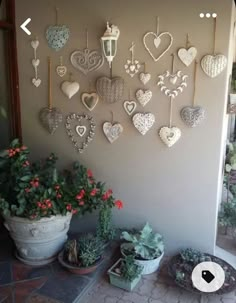 many heart shaped ornaments are hanging on the wall next to potted plants and succulents