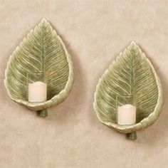 two green leaf shaped wall sconces with candle holders on each side, one holding a lit candle