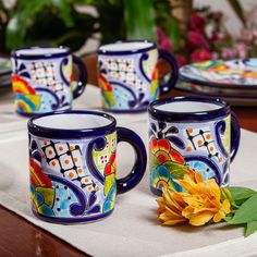 three coffee mugs sitting on top of a table next to a yellow flower