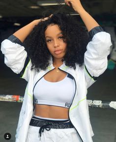 a woman with curly hair is posing for the camera and holding her hands behind her head