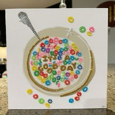 a white card with colorful beads on it and a spoon sticking out of the middle