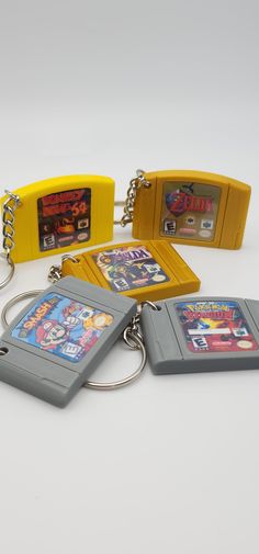 four gameboy key chains are sitting on a white surface, one is yellow and the other is gray