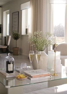 a living room filled with furniture and a glass table topped with two glasses of wine