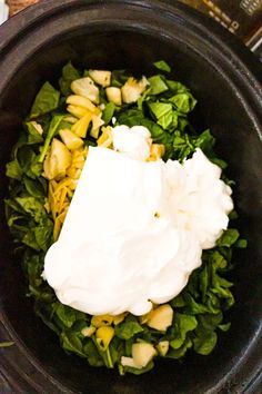 a black bowl filled with greens and whipped cream