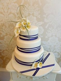 a three tiered wedding cake with blue ribbon and white flowers on the top layer