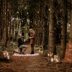 a man kneeling down next to a woman on a blanket in the middle of a forest