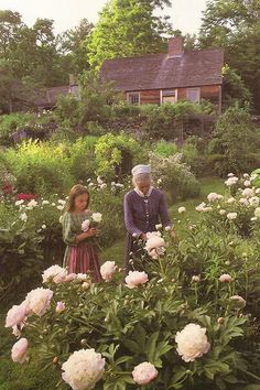 an old man and woman standing in the middle of a garden next to some flowers